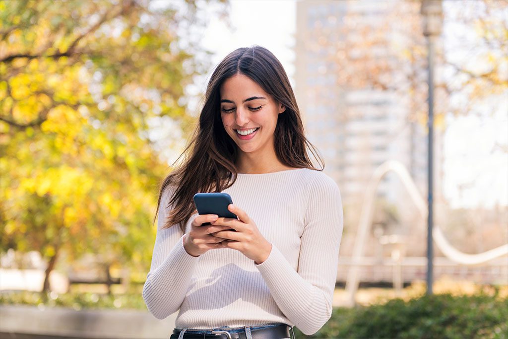 Frau blickt unterwegs auf ihr Smartphone und prüft ihr Zuhause